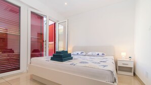 A bedroom with a bed, a nightstand, a lamp, and a window with blinds. - Apartment Dora Pag (Pag)
