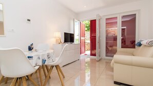 A modern living room with a white sofa, a dining table with chairs, and a TV. - Apartment Dora Pag (Pag)