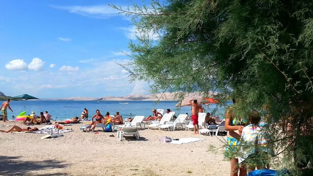 A beach with sun loungers and umbrellas, a clear sky, and a calm sea. - Apartment Dora Pag (Pag)