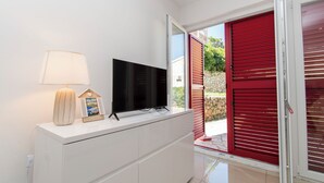 A modern room with a flat-screen TV on a white cabinet, a lamp, and a red door. - Apartment Dora Pag (Pag)