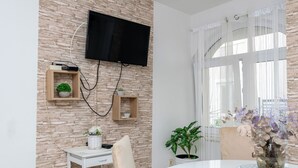 A modern living room with a stone wall, a mounted TV, and a dining area with a round table and chairs.