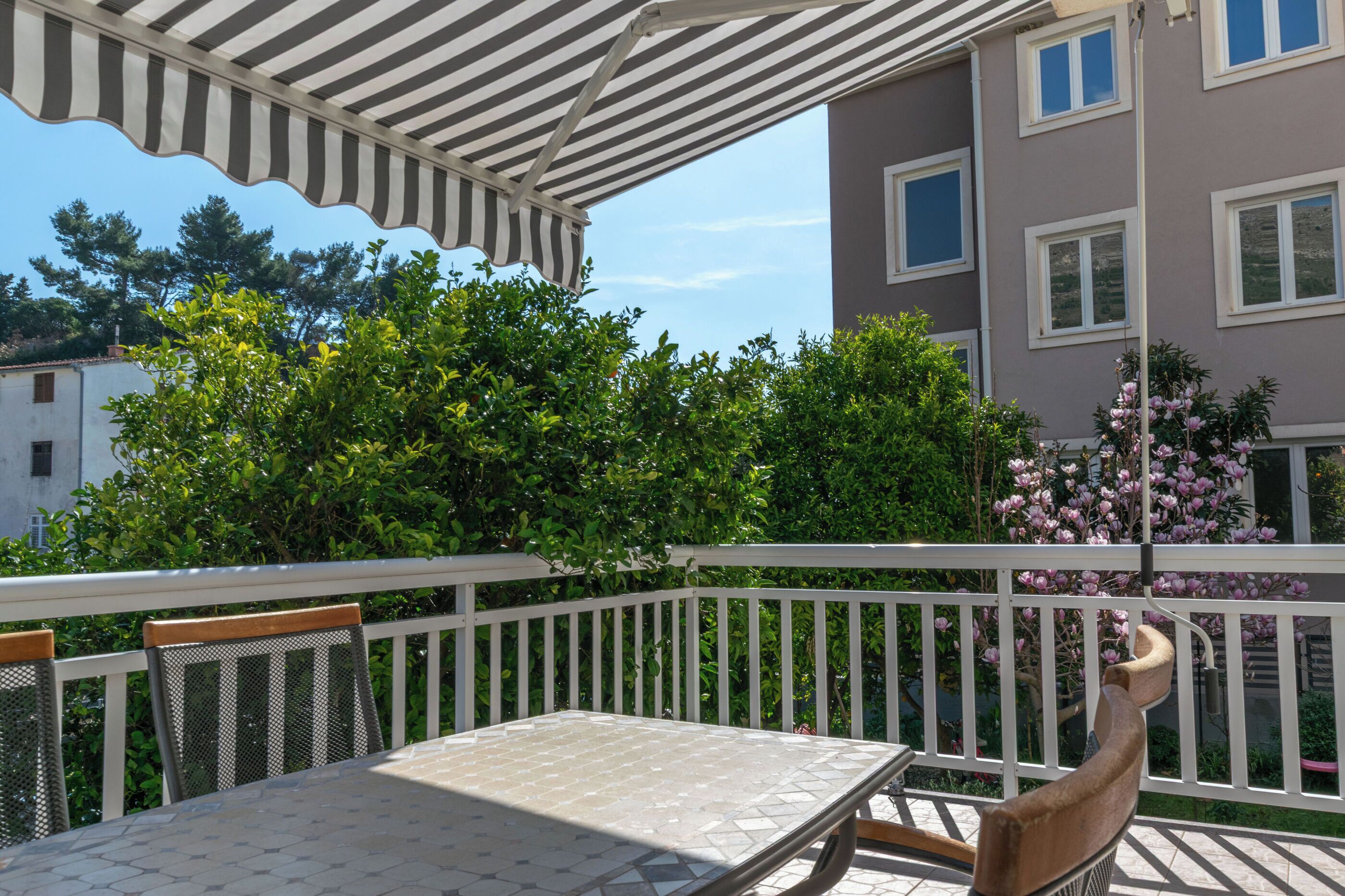 A balcony with a striped awning, a table, and chairs.