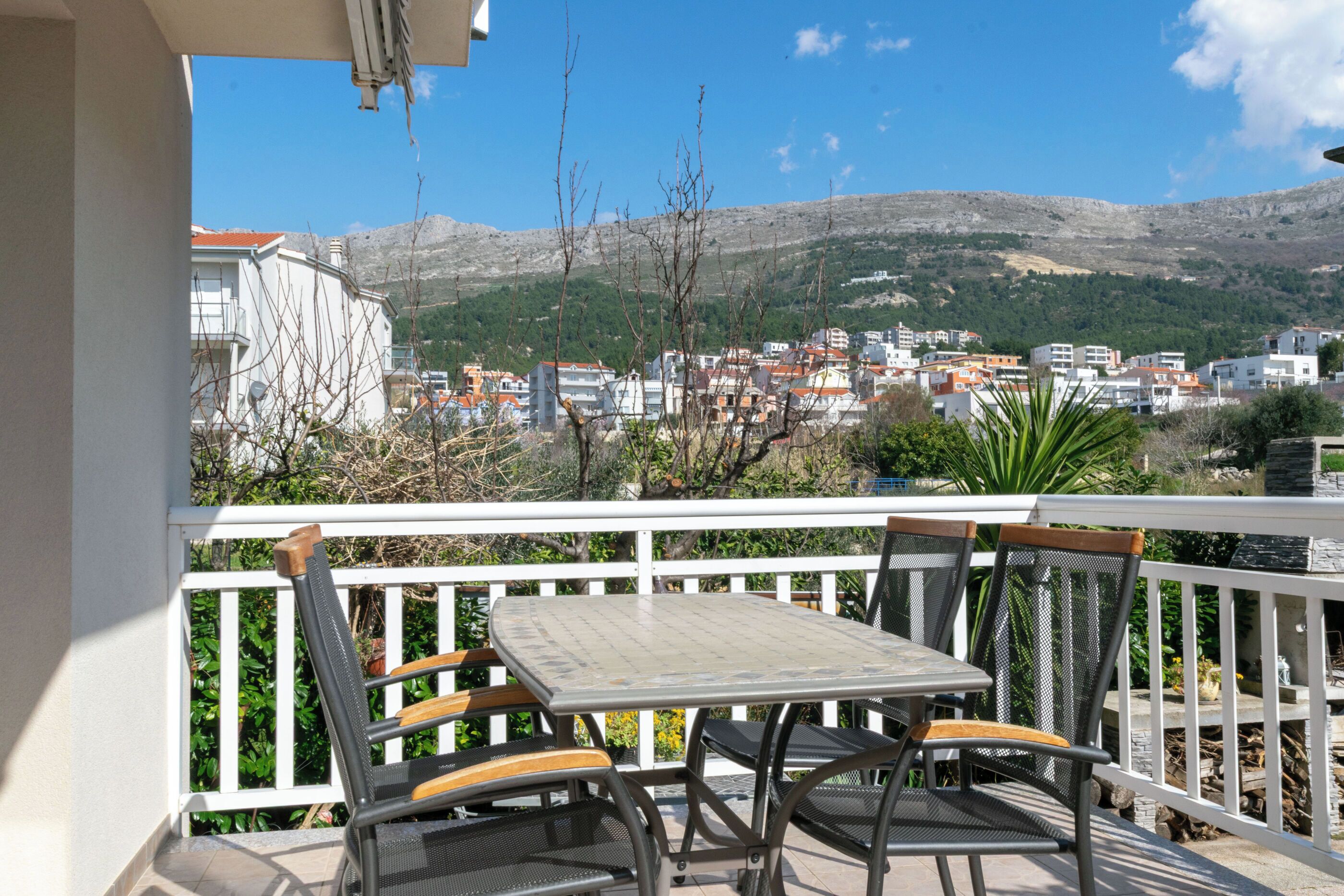 A balcony with a table and chairs, overlooking a town and mountains.