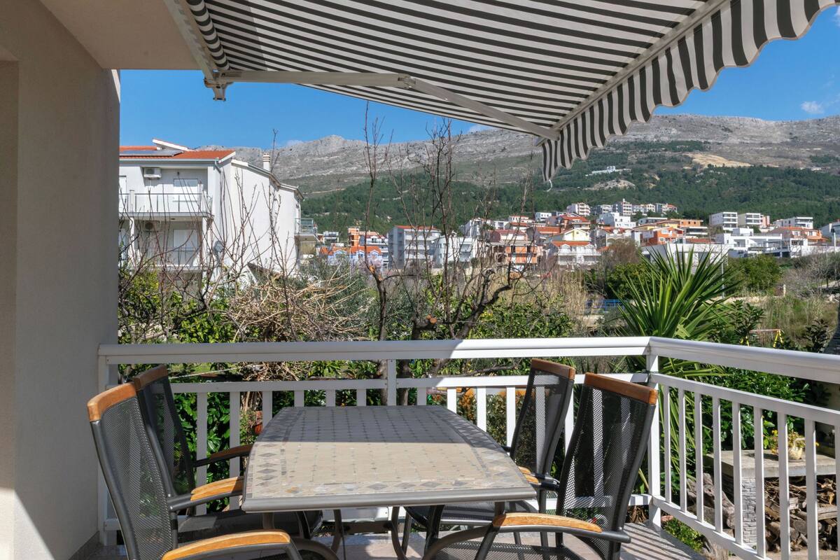 A balcony with a table and chairs, overlooking a town with buildings and mountains in the background.