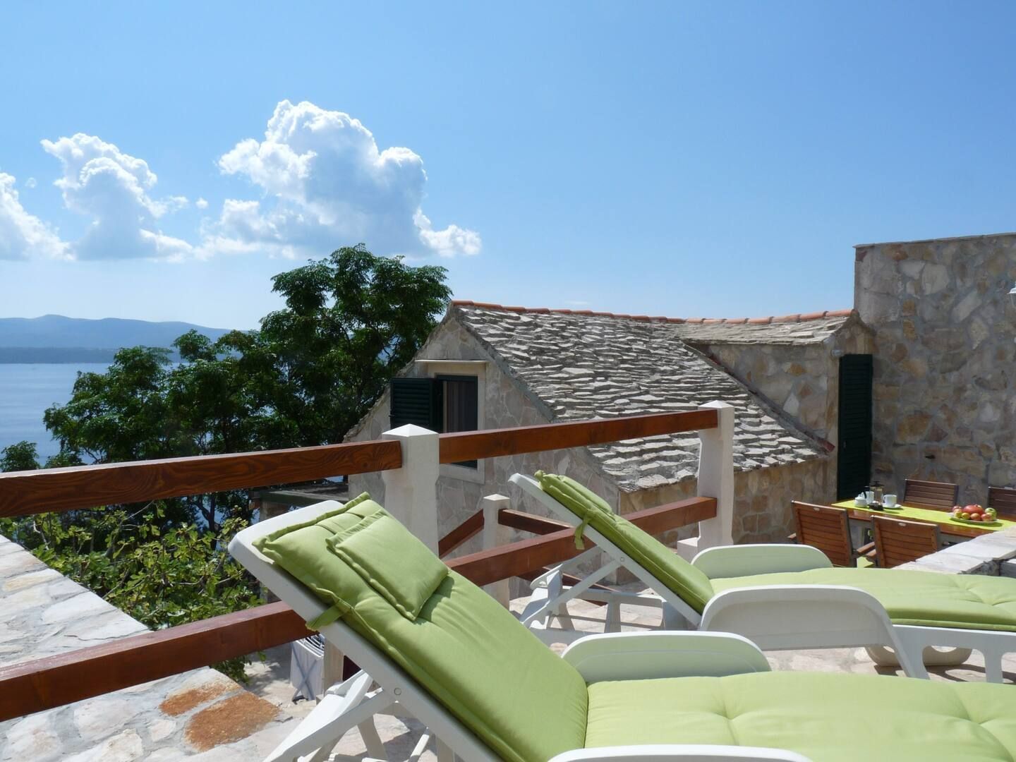 A terrace with lounge chairs and a table, overlooking a body of water and a mountainous landscape.