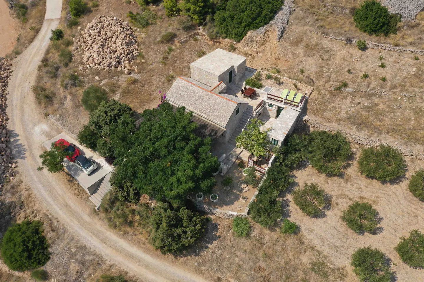 Vista aerea di un edificio in pietra con tetto piatto, circondato da alberi e un sentiero sterrato.