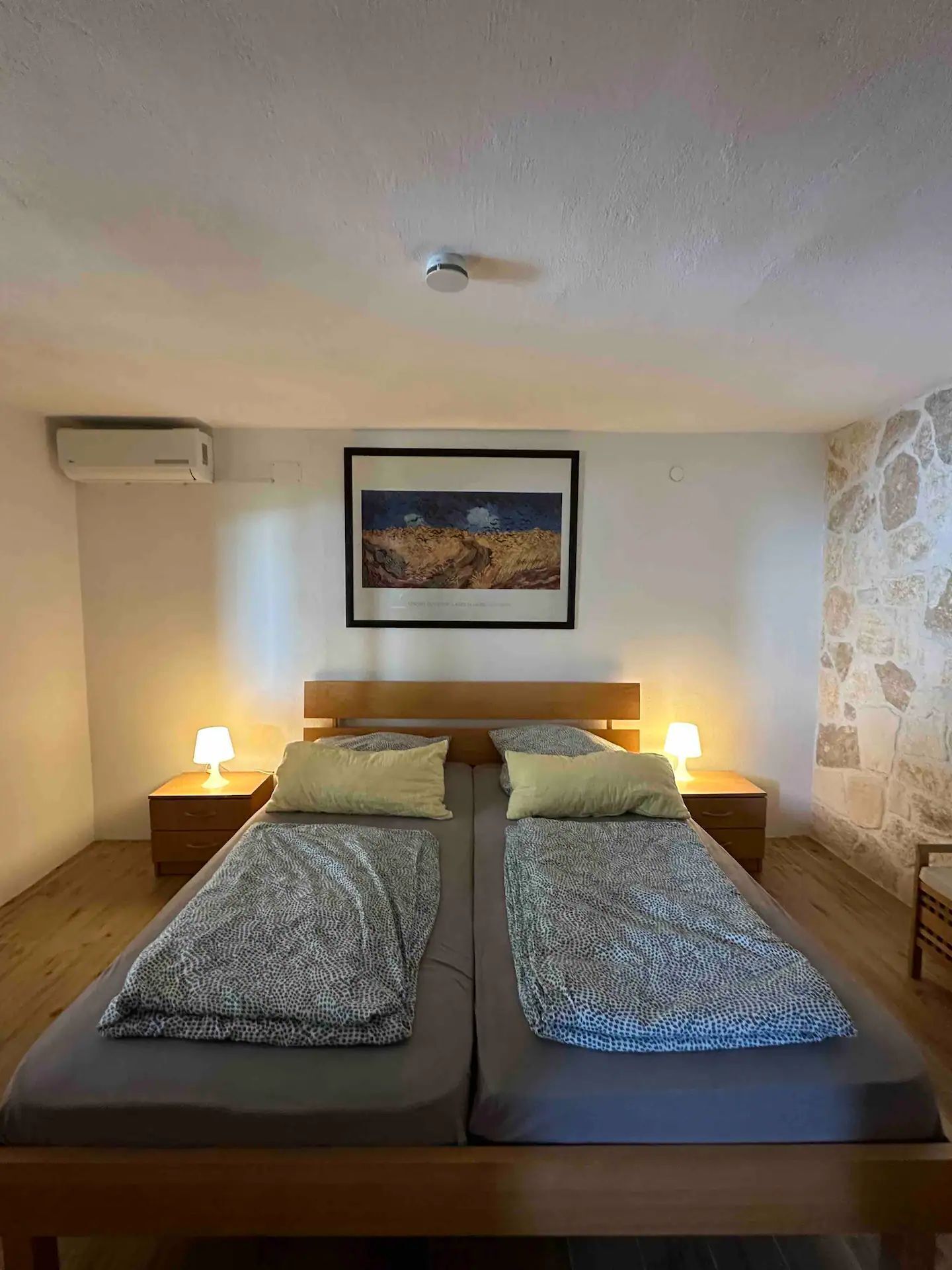 A twin room with two beds, a framed painting on the wall, and a stone wall on one side.