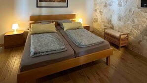 Un dormitorio con una cama de madera, dos mesitas de noche con lámparas, una pared de piedra y un cuadro enmarcado.