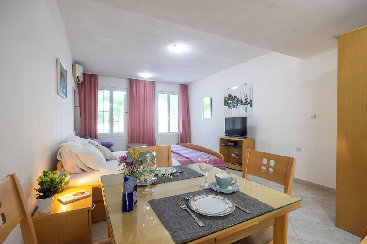 A neatly arranged hotel room with a bed, a TV, a dining table set for two, and a small seating area.