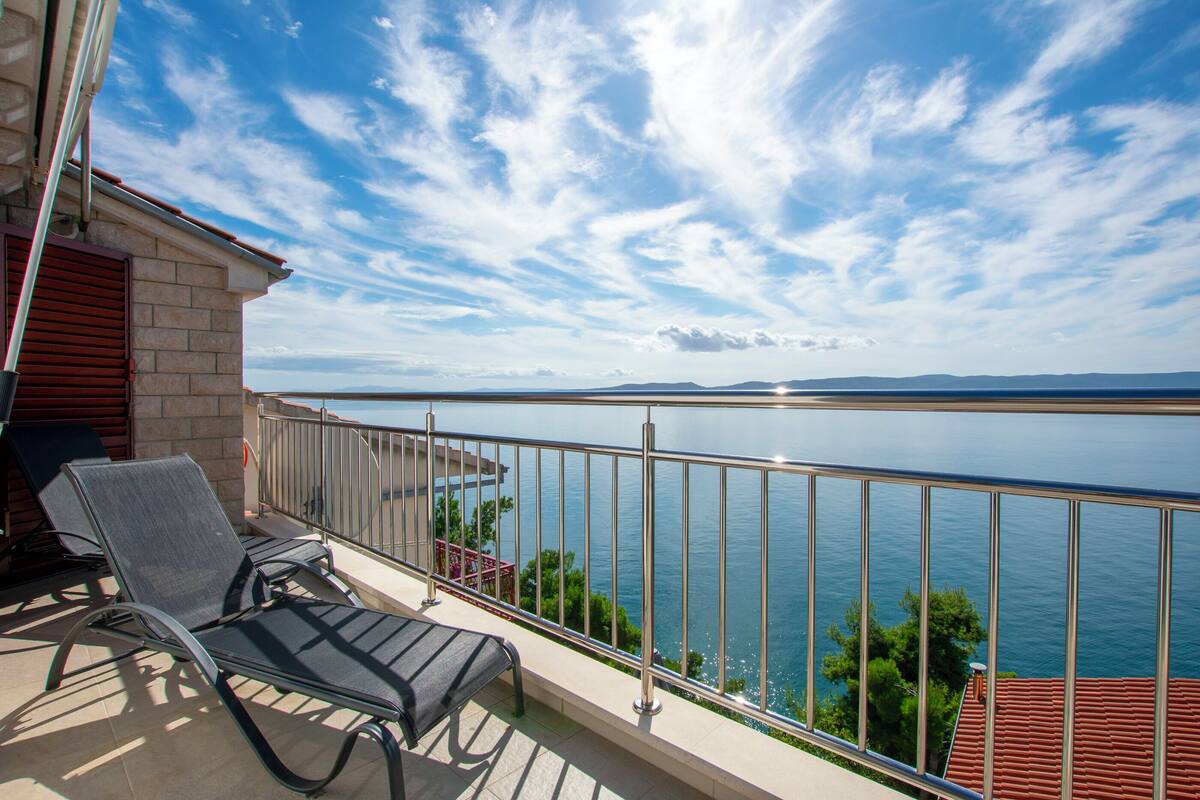A balcony with two lounge chairs overlooking a body of water and distant mountains.