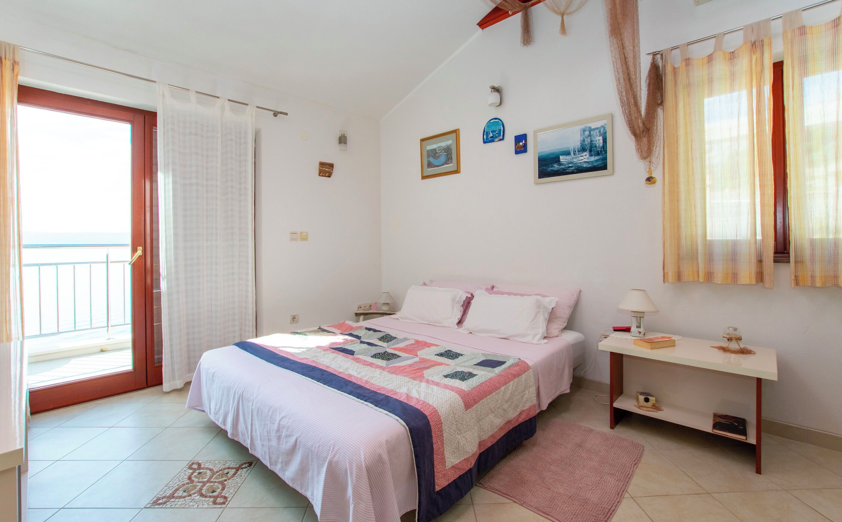 Ein Schlafzimmer mit Bett, Nachttisch und Meerblick durch eine Balkontür.