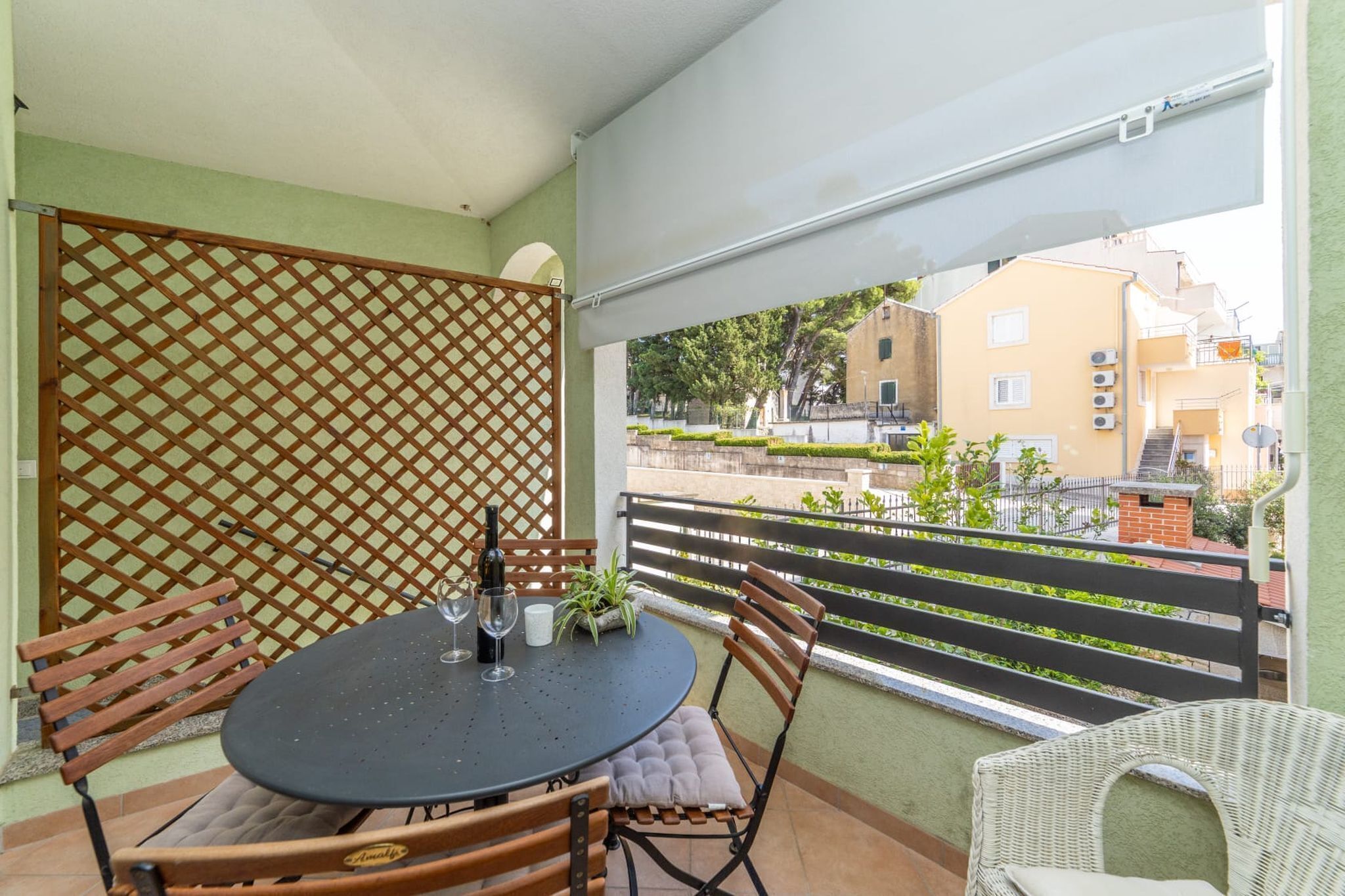 A balcony with a round table, chairs, and a view of buildings and greenery.