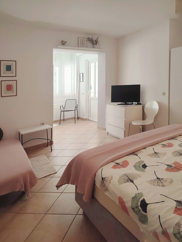 Ein Schlafzimmer mit einem Bett, einem Schreibtisch, einem Sessel, einem Fernseher und einer Tür zu einem anderen Raum.