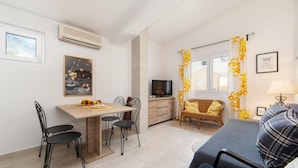 Un espace de vie compact comprenant un coin repas, un canapé, un téléviseur et une fenêtre avec des rideaux.