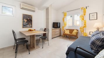 Un espacio habitable compacto con zona de comedor, un sofá, un televisor y una ventana con cortinas.