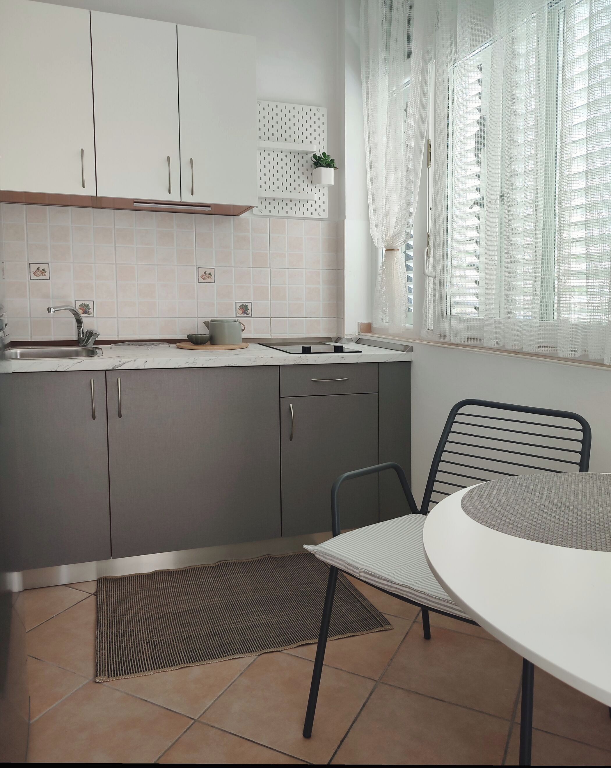 Una cocina moderna con armarios grises, encimera blanca y un pequeño comedor con una mesa redonda y sillas.