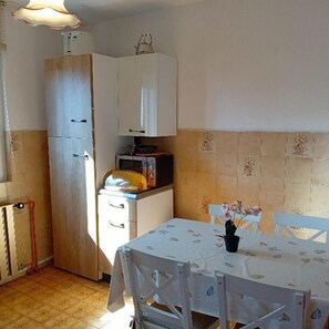 A compact kitchen with a refrigerator, microwave, and a table with chairs. - Apartment Sunset Lina (Pula)