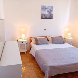 A bedroom with a bed, two bedside tables, a nightstand, a painting on the wall, and a wooden floor. - Apartment Sunset Lina (Pula)