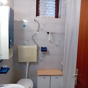 Ein kleines Badezimmer mit Toilette, Waschbecken, Dusche und Fenster.