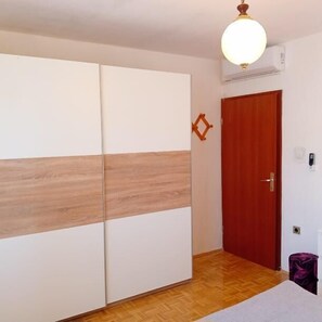 A room with a wardrobe, a wooden floor, a red door, and a ceiling light fixture. - Apartment Sunset Lina (Pula)
