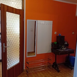 A room with a wooden door, a whiteboard, a small table with decorative items, and a metal rack. - Apartment Sunset Lina (Pula)