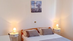 Ein Schlafzimmer mit einem Bett, zwei Nachttischen mit Lampen, einem kleinen Tischchen, einem Wandbild und Holzboden.