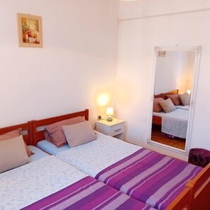 Ein Schlafzimmer mit zwei Betten, einem Nachttisch mit Lampe, einem Spiegel und einem gerahmten Bild an der Wand.