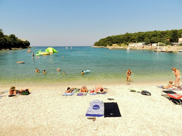 A beach with clear water, people swimming and sunbathing, and a few boats in the distance. - Apartment Sunset Lina (Pula)