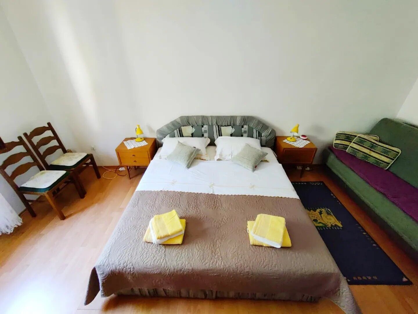 A bedroom with a bed, two bedside tables, a chair, a green sofa, and a wooden floor.
