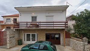 Una casa a due piani con un balcone, un garage e un'auto verde parcheggiata davanti.