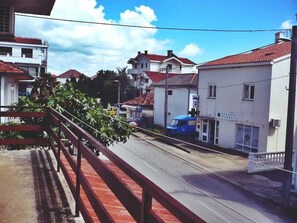A street view with buildings, a blue truck, and a red railing. - Apartment Travica (Posedarje)
