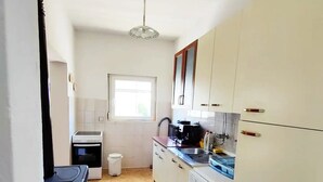 Una cucina con mobili bianchi, una finestra, una ventola a soffitto e un pavimento piastrellato.