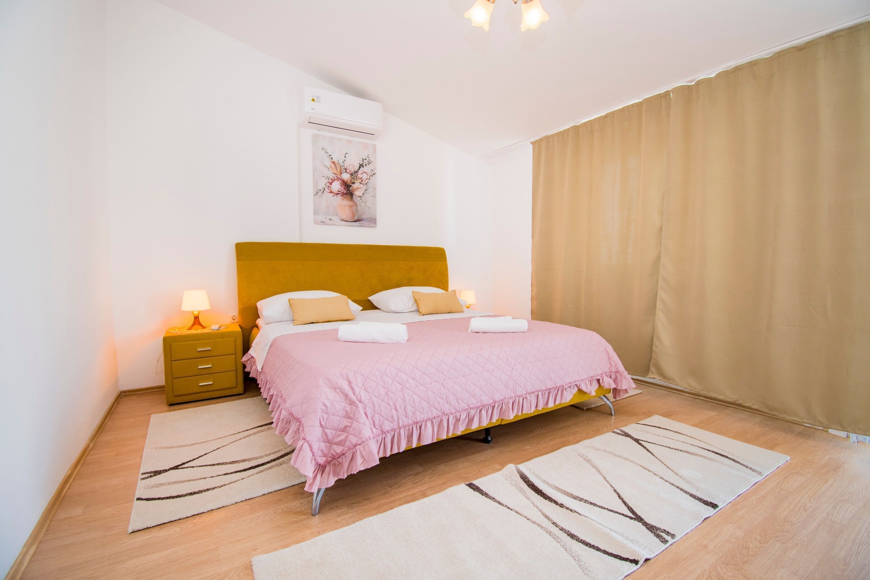 A neatly arranged bedroom with a bed, bedside lamps, a nightstand, and a wall-mounted air conditioner.