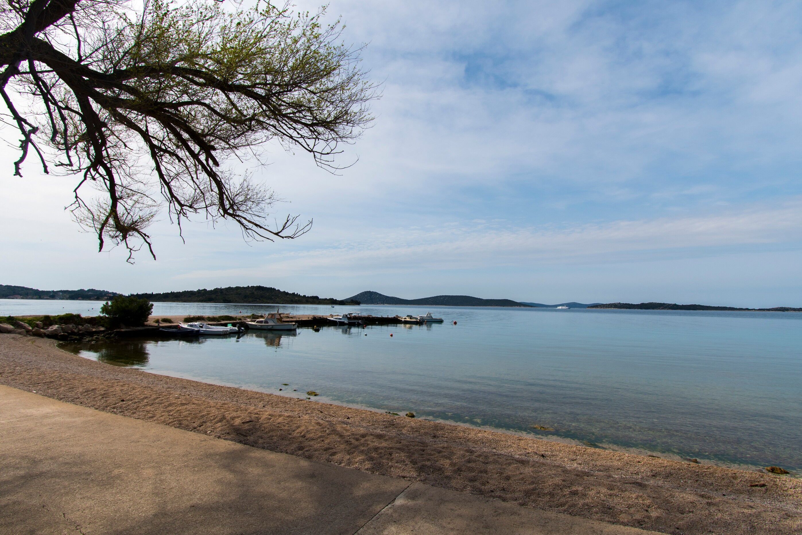 A calm lake with boats docked at a pier, surrounded by hills and a clear sky.