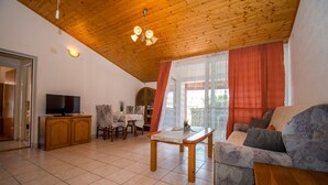 A living room with a wooden ceiling, a television, a sofa, a table, and a window with curtains. - Apartments Neve (Vodice)
