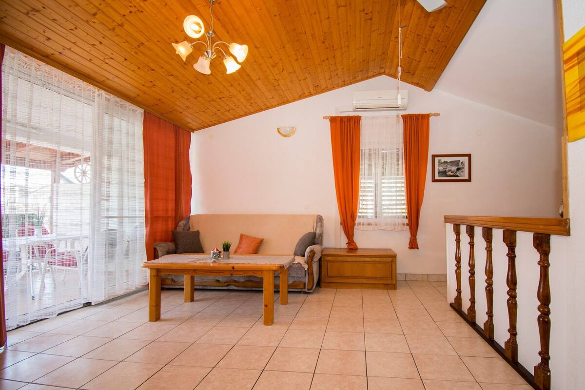 A spacious living room with a wooden ceiling, a sofa, a coffee table, and a view of the outside through large windows.