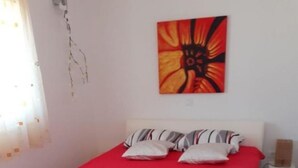 A bed with a red bedspread, white pillows, and a small white rug on a wooden floor. - Apartment Jasmina (Nin)