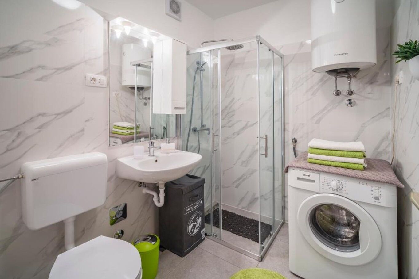 Un bagno moderno con doccia vetrata, lavandino, water e lavatrice.