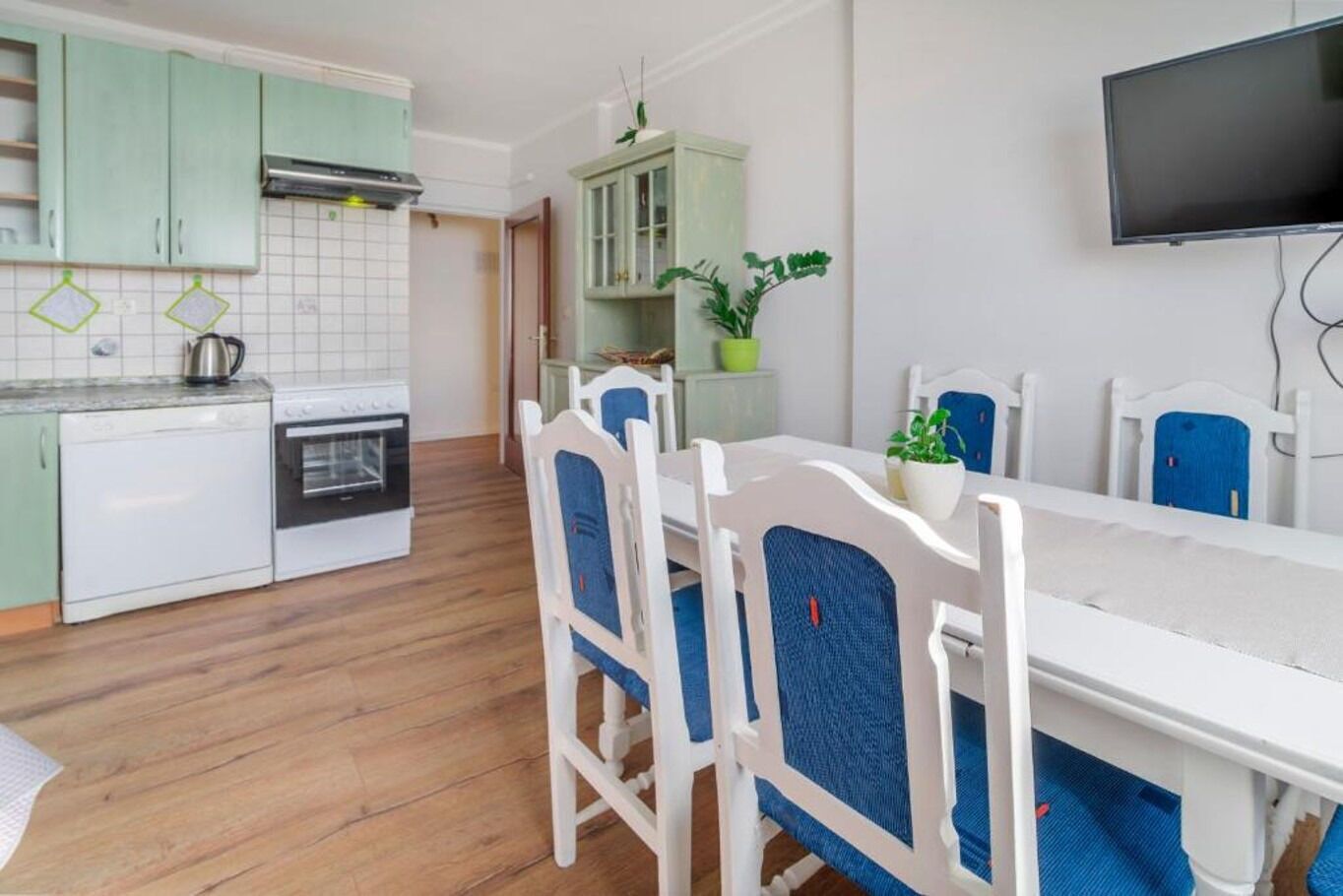 Une cuisine compacte avec un coin repas, comprenant une table et des chaises blanches, un petit réfrigérateur et une cuisinière.