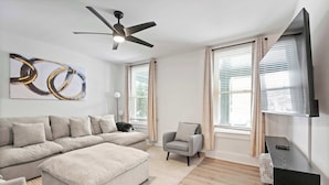 Una sala de estar moderna con un sofá modular, un sillón pequeño, un televisor de pantalla plana y un ventilador de techo.