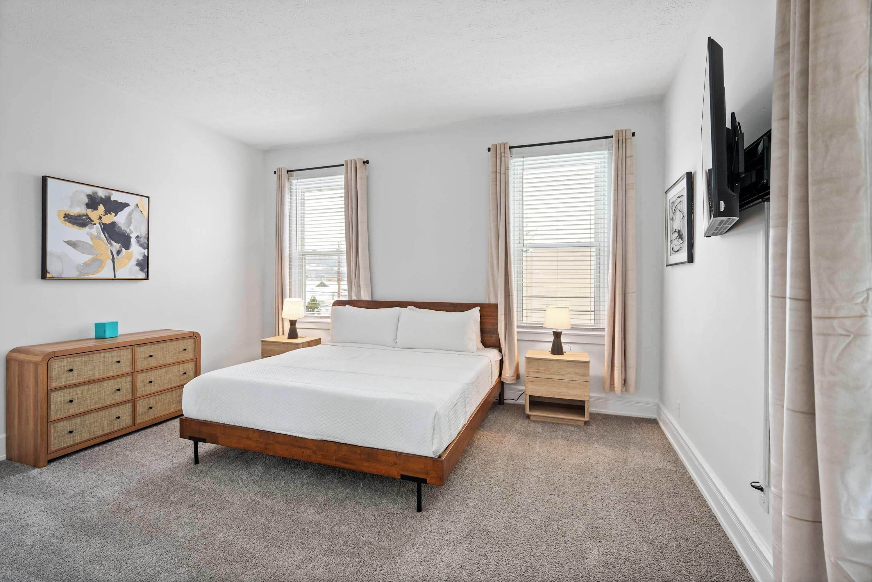 A bedroom with a wooden bed, two bedside tables, a dresser, and a wall-mounted air conditioning unit.