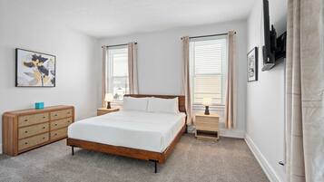 A bedroom with a wooden bed, two bedside tables, a dresser, and a wall-mounted air conditioning unit.