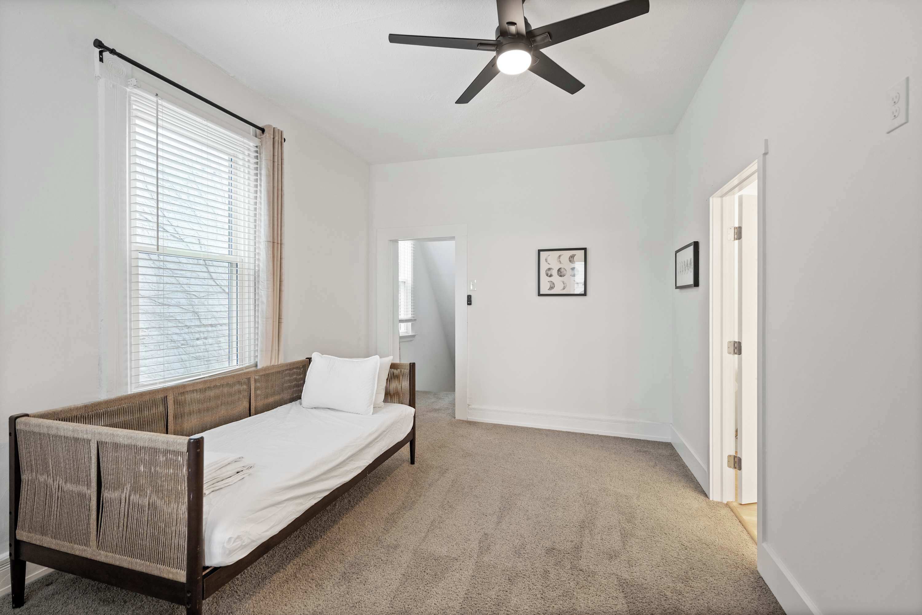 A bedroom with a single bed, a ceiling fan, and a door leading to another room.