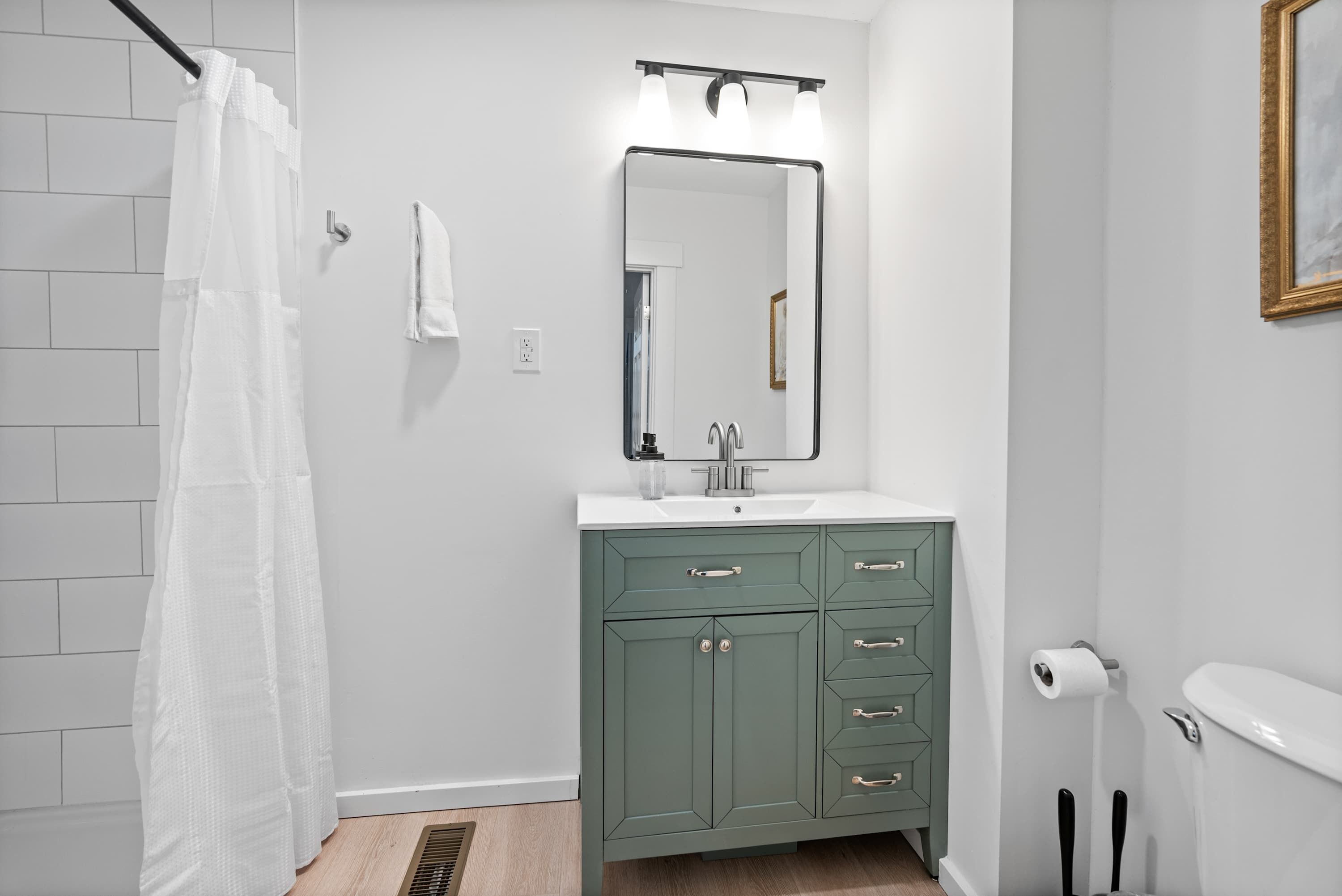 Un baño con cortina de ducha blanca, un lavabo con espejo y un inodoro.