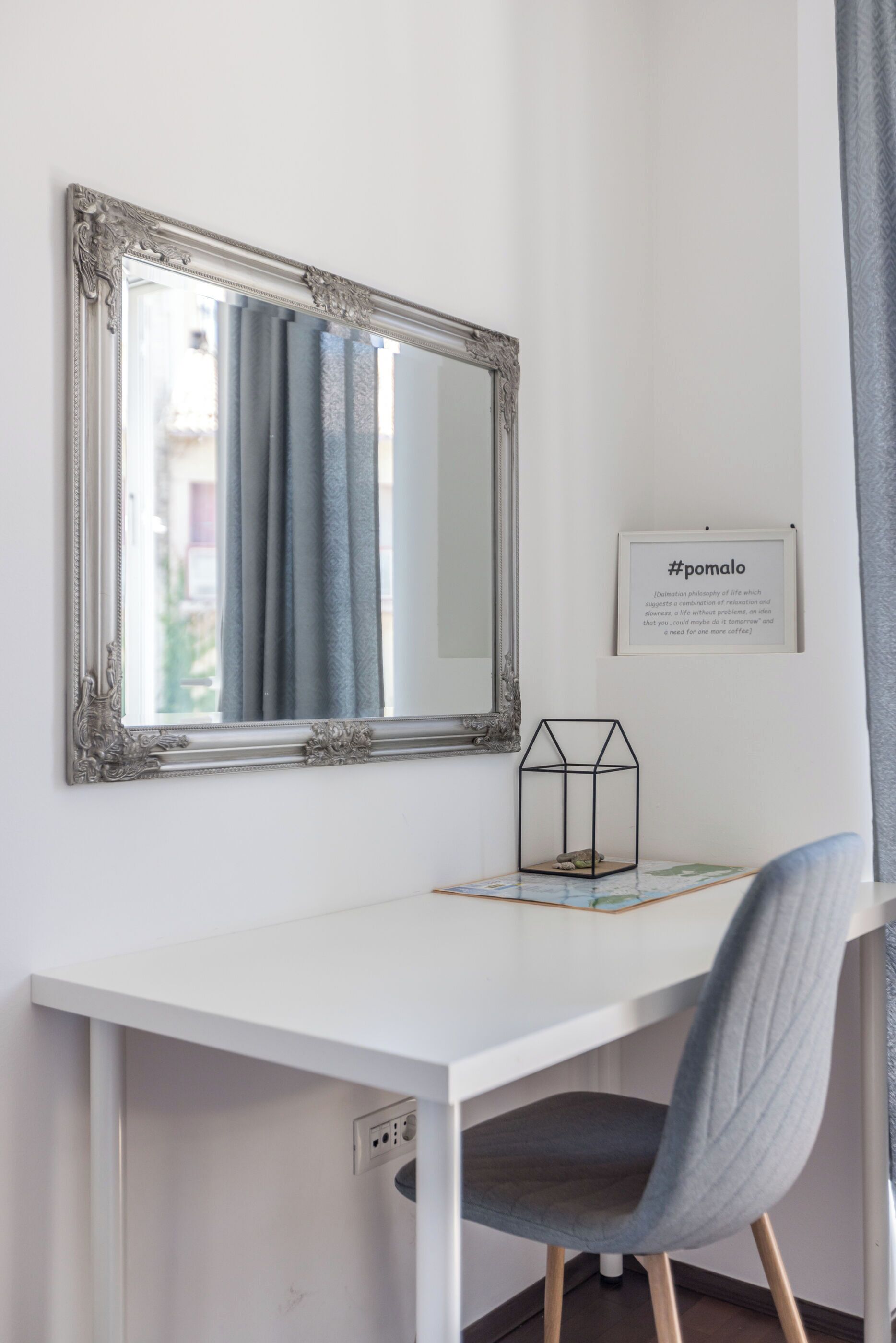 A white desk with a chair, a mirror, and a framed quote on the wall.
