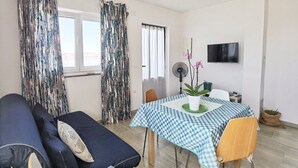 A room with a sofa, a table with a checkered tablecloth, a potted plant, and a TV on the wall. - Apartments Adria (Karlobag)