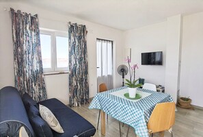A room with a sofa, a table with a checkered tablecloth, a potted plant, and a TV on the wall. - Apartments Adria (Karlobag)