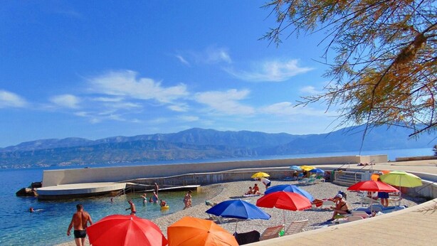 A beach with clear water, umbrellas, and people.