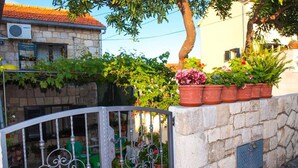 A stone wall with a metal gate, potted plants, and a building with a tiled roof.