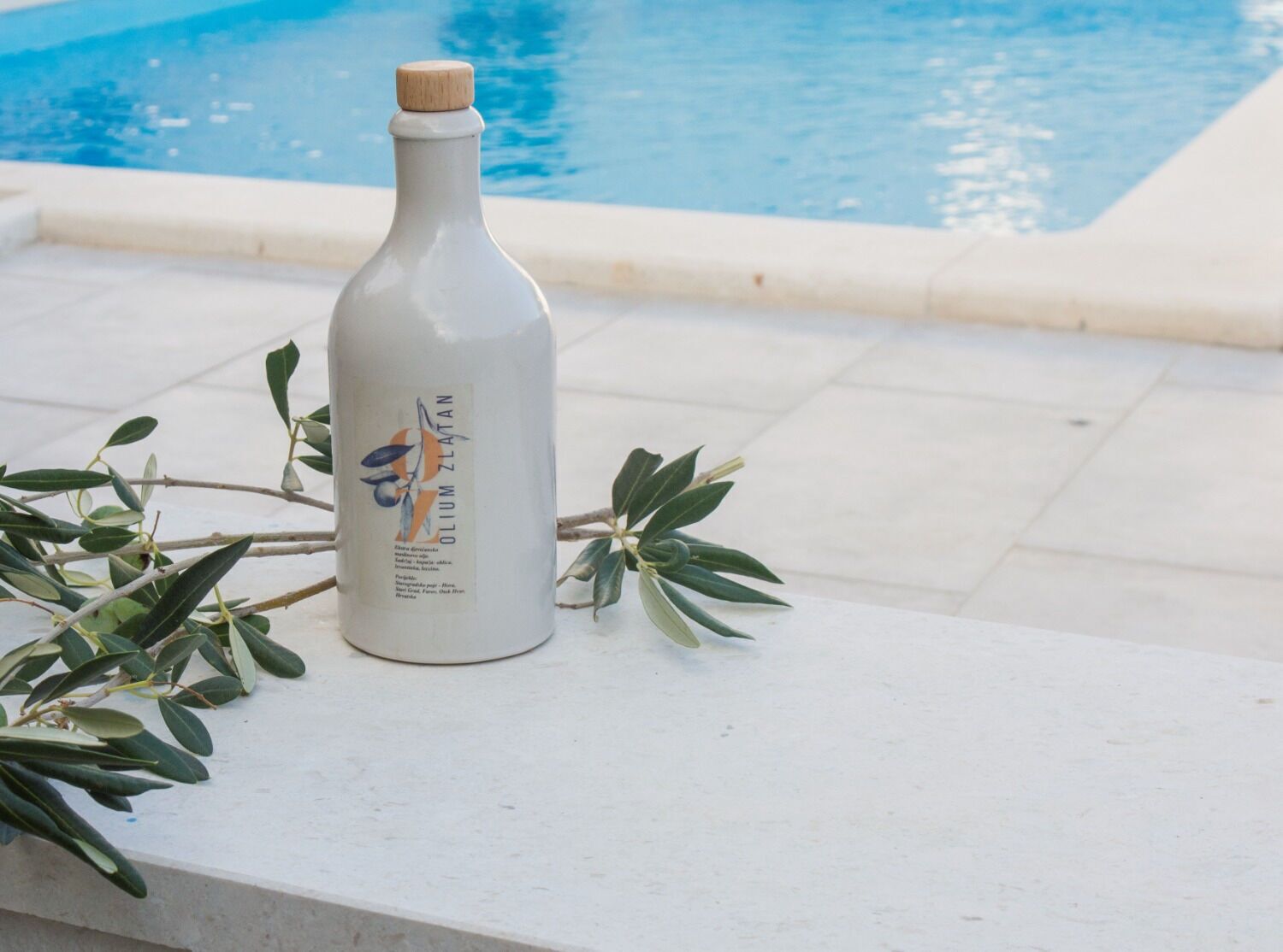 A bottle of Oilium Zlatan olive oil by the poolside.